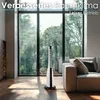 A modern tower fan is positioned in a bright, sunlit living room with large windows overlooking lush greenery. Voir les images du produit