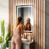 A woman is applying makeup in front of a lighted mirror in a modern bathroom. Podgląd zdjęcia produktu