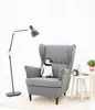 A plush penguin sits on a gray armchair next to a floor lamp and a small side table with decorative items. Podgląd zdjęcia produktu