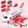 A toy transport airplane with several smaller toy fire rescue vehicles arranged around it, along with miniature traffic signs and trees. Produktbild-Vorschau