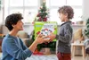 A mother gives a wooden train track toy to her son in a living room decorated for Christmas. Produktbild-Vorschau