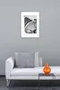A framed picture of a modern building hangs on a gray wall above a white sofa with a gray pillow and an orange vase on a small black table. Anteprima dell’immagine prodotto