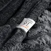 A close-up of a gray, fuzzy blanket with a tag attached. Produktbild-Vorschau