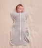 A baby sleeping in a swaddle sack on a beige surface. Produktbild-Vorschau