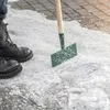 A person is using an ice scraper to clear snow and ice from a paved walkway. Produktbild-Vorschau