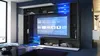 A modern living room with a wall-mounted entertainment unit featuring a large TV and integrated shelving, illuminated by blue LED lights. Produktbild-Vorschau
