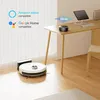 A robot vacuum cleaner is shown on a wooden floor next to its charging station, with a desk and a smart speaker in the background. Náhled obrázku produktu