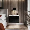 A bedside table with a lamp and decorative items next to a bed in a bedroom.