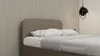 A close-up view of a bed with a brown upholstered headboard and white bedding, set against a wall with vertical paneling. Produktbild-Vorschau