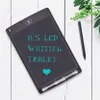 A black LCD writing tablet with teal text and a teal heart is placed on a white wooden surface, next to a green leafy branch and a stylus. Anteprima dell’immagine prodotto