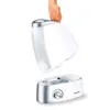 A hand is holding the top part of a white humidifier, showing it detached from the base. Podgląd zdjęcia produktu
