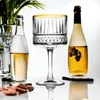 A still life arrangement of two bottles of champagne and a champagne coupe glass, with some dark berries and chocolate pieces in the foreground. Podgląd zdjęcia produktu