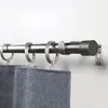 A close-up view of a metal curtain rod with rings and attached grey fabric curtains, mounted on a white wall. Produktbild-Vorschau
