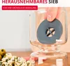 A hand is holding a gray sieve inside a glass jar, with food items in the foreground. Anteprima dell’immagine prodotto