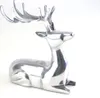 A polished silver aluminum sculpture of a reclining deer with antlers, set against a white background. Produktbild-Vorschau