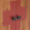 A close-up view of two cabinet doors with dark knobs, painted with a red cross shape. Náhľad obrázku produktu