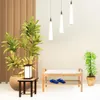 A shoe rack with a seat and cushion, along with two pairs of blue flip-flops, is shown in a room with plants and pendant lights. Produktbild-Vorschau