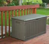 A brown plastic storage box sits on a wooden deck next to a wooden railing, with a garden in the background. Produktbild-Vorschau