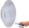 A hand holds a remote control, pointing it towards a white LED lamp. Produktbild-Vorschau