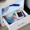 A close-up view of a white, high-gloss nightstand with an open drawer, showing books and decorative items inside, illuminated by blue LED lighting. Produktbild-Vorschau