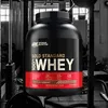 A large tub of protein powder is shown in a gym setting. Produktbild-Vorschau