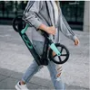 A person is walking outdoors carrying a folded scooter. Voir les images du produit
