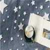 A close-up view of a soft blanket with a star pattern, a book, and a cup and saucer. Anteprima dell’immagine prodotto