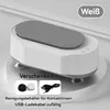 A white and gray ultrasonic cleaning machine for contact lenses with a USB charging cable and two lens cases. Produktbild-Vorschau