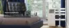 A portable air conditioner is shown in a bedroom setting, next to a window with a view of trees. Produktbild-Vorschau