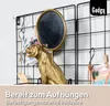 A close-up of a black metal grid wall organizer with decorative items attached, including a golden tiger statue with a mirror and some cards. Produktbild-Vorschau