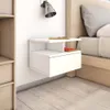 A white hanging nightstand with a drawer and an open shelf, mounted on a white wall next to a bed. Náhled obrázku produktu
