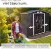 A man is pushing a wheelbarrow with a hose towards a garden shed. The shed is open, showing tools inside. There are trees and bushes in the background. Produktbild-Vorschau