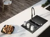 A modern kitchen counter with a black sink, faucet, and cups, next to a bowl of cookies and a wooden floor with a chair. Produktbild-Vorschau