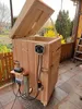 A wooden electric smoking chamber with a control panel and power cords attached, situated outdoors on a patio. Náhled obrázku produktu
