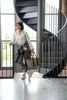 A woman stands next to a spiral staircase, holding a leopard-print bag. Náhled obrázku produktu