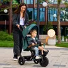 A woman pushing a child on a tricycle in an outdoor urban setting. Produktbild-Vorschau