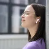 A young woman wearing glasses and pink earbuds leans against a pole, eyes closed, enjoying music. Produktbild-Vorschau