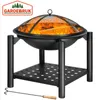 A black metal fire pit with a mesh cover and burning wood inside, resting on a stand with a lower shelf. A poker tool is placed on the ground in front of the stand. Produktbild-Vorschau