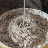 A close-up view of a cement mixer attachment in a bucket of concrete. Náhled obrázku produktu