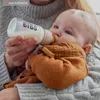 A person is holding a baby and feeding it with a bottle. Anteprima dell’immagine prodotto