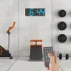 A home gym setup with an exercise bike, a bench, and weight plates on the wall. A hand is holding a remote control. Náhled obrázku produktu