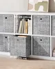 A white shelving unit with gray fabric storage boxes. Some boxes are open, revealing books and other items. Dimensions are indicated with white lines and text. Produktbild-Vorschau