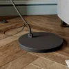 Close-up of the base and stem of a black floor lamp on a wooden floor, with a portion of a gray sofa visible on the right. Produktbild-Vorschau