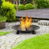 A fire pit with burning logs sits on a stone patio in a garden setting, with lush greenery and a wooden deck in the background. Anteprima dell’immagine prodotto