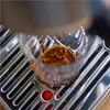 A close-up shot of espresso being brewed in a clear glass cup, with the espresso machine's drip tray visible below. Produktbild-Vorschau