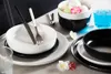 A table setting with white and black ceramic dishes, cutlery, and a glass of blue liquid. Voir les images du produit