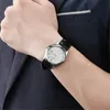 A man's wrist wearing a silver watch with a black leather strap, partially covered by a dark blue jacket. Podgląd zdjęcia produktu
