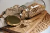 A glass jar of oats is tipped over on a wooden cutting board, with a golden spoon and lid nearby. Produktbild-Vorschau