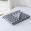 A folded gray blanket with a ribbed texture is placed on a white bed. Produktbild-Vorschau