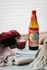 A bottle of Rotbäckchen Immunstark juice with a glass of the juice, a knitted hat, and a blanket. Produktbild-Vorschau